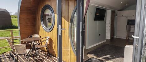 A modern RV with a wooden exterior, a dining area with a table and chairs, and a television mounted on the wall.