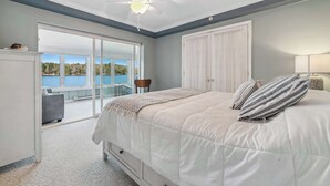 Een slaapkamer met een groot bed, een plafondventilator, uitzicht op de omgeving en een schuifdeur naar een balkon.