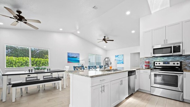 A modern kitchen with white cabinetry, a granite countertop, a built-in oven, and a microwave. - The Jupiter Hideaway (Jupiter)