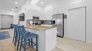 A modern kitchen with white cabinets, a stainless steel refrigerator, and a granite countertop. - The Jupiter Hideaway (Jupiter)