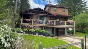 A two-story log cabin with a balcony decorated with red, white, and blue bunting. - Lakefront Cottage on Java Lake (Arcade)