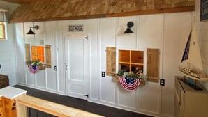 A boat house with a wooden ceiling, a door labeled "BOAT HOUSE", and two windows with American flags and flowers. - Lakefront Cottage on Java Lake (Arcade)