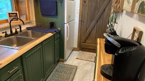 A kitchen with green cabinets, a white refrigerator, a coffee maker, and a rustic wooden door. - Lakefront Cottage on Java Lake (Arcade)