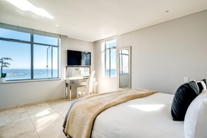 Hotellihuone, jossa on sänky, työpöytä, tuoli, televisio ja suuri ikkuna, josta avautuu näkymä merelle.
