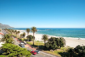 A coastal road with palm trees, a beach, and a clear blue sky. - Ocean View Camps Bay 3bed Apt Beach Vistas (Cape Town)