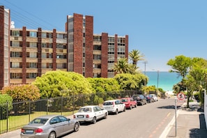 Un edificio a più piani con facciata in mattoni e balconi, situato vicino alla costa, con auto parcheggiate e cielo sereno.