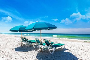 Une plage avec quatre chaises longues et deux parasols.