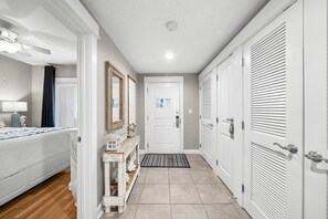 A hallway with a bed, a console table, a door with a notice, and a door with louvered panels. - Grand Panama FREE Beach Service, Gulf Views, Heated Pool, Grills, FREE Golf! (Panama City Beacu)