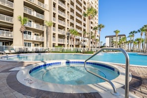 A hotel pool area with a hot tub, palm trees, and a multi-story building with balconies.
