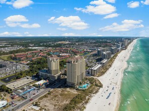 An aerial view of a coastal city with a beachfront, high-rise hotels, and a large parking area. - Grand Panama FREE Beach Service, Gulf Views, Heated Pool, Grills, FREE Golf! (Panama City Beacu)