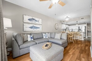 A modern living room with a grey sectional sofa, a wooden coffee table, and a ceiling fan. - Grand Panama FREE Beach Service, Gulf Views, Heated Pool, Grills, FREE Golf! (Panama City Beacu)