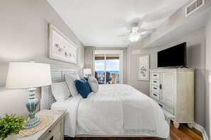 Une chambre à coucher avec un lit, une télévision, un ventilateur de plafond et une vue sur l’extérieur.