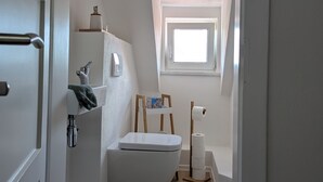 A narrow, white-walled bathroom with a toilet, sink, and window.