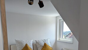 A bedroom with a bed, two pillows, a blanket, a window, and a ceiling light fixture.