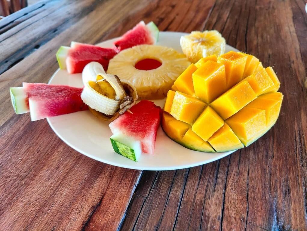 A plate of sliced fruits including watermelon, pineapple, mango, and banana on a wooden table.