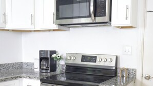 Una cocina con gabinetes blancos, un microondas de acero inoxidable, una estufa a gas y un horno empotrado.