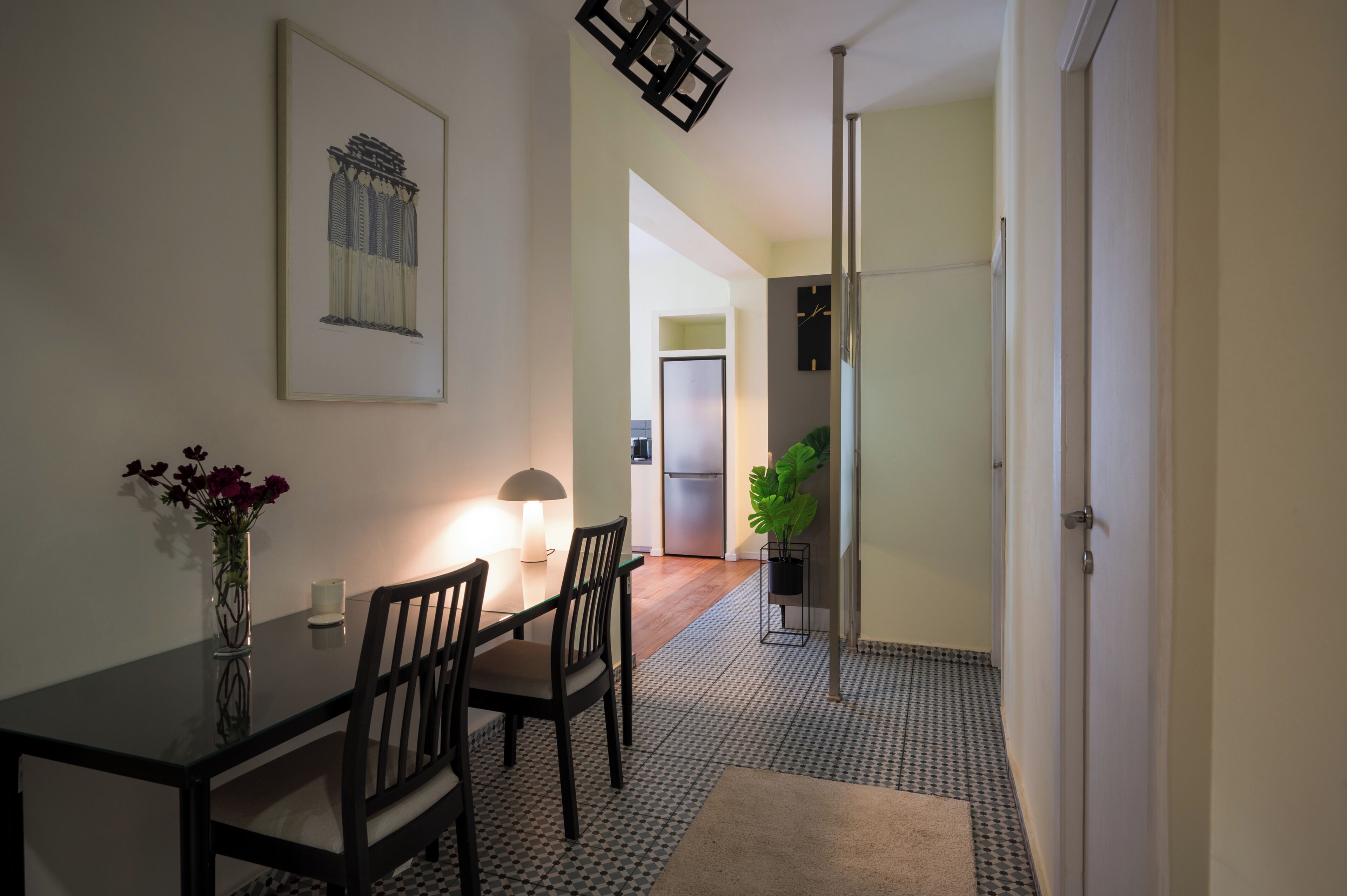 Un coin repas comprenant une table, des chaises, un vase de fleurs, une lampe et un tableau encadré accroché au mur.