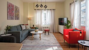 A modern living room with a grey sofa, a red armchair, a small round table, and a TV. - Mia Homes - Heart of Athens, Mia Homes (Athens)