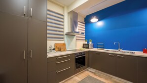 A modern kitchen with grey cabinets, a stainless steel sink, and a blue accent wall. - Mia Homes - National Museum, Mia Homes (Athens)