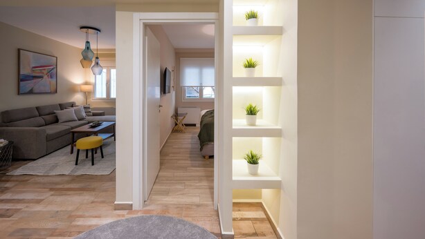 A modern living room with a sofa, coffee table, and pendant lights. There is a hallway leading to another room with a bed and a window. - Mia Homes - National Museum, Mia Homes (Athens)