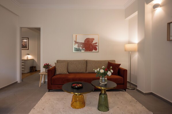 A modern living room with a brown sofa, two round tables, a vase with flowers, and a framed picture on the wall.