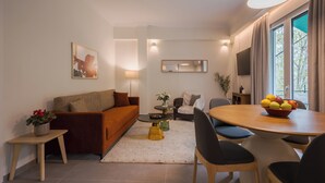 Un salon moderne comprenant un canapé, une table basse, une table à manger et des chaises. Un téléviseur est fixé au mur et il y a une fenêtre avec des rideaux.
