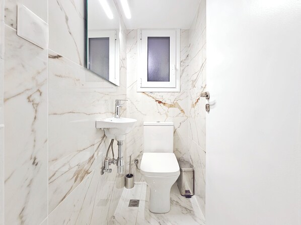 Un baño moderno con suelo de mármol blanco, un lavamanos blanco, un inodoro y un espejo sobre el lavamanos.