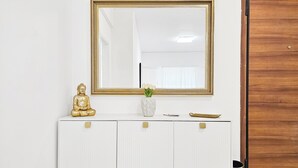 A white vanity with a gold Buddha statue, a vase with white flowers, and a small tray.