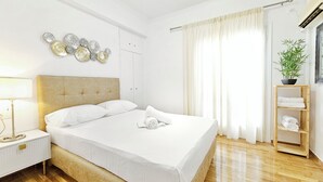 A neatly arranged bedroom with a bed, bedside table, lamp, and a shelf with towels.