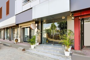 Um edifício moderno com entrada de vidro, degraus que levam à porta e plantas em vasos no chão.