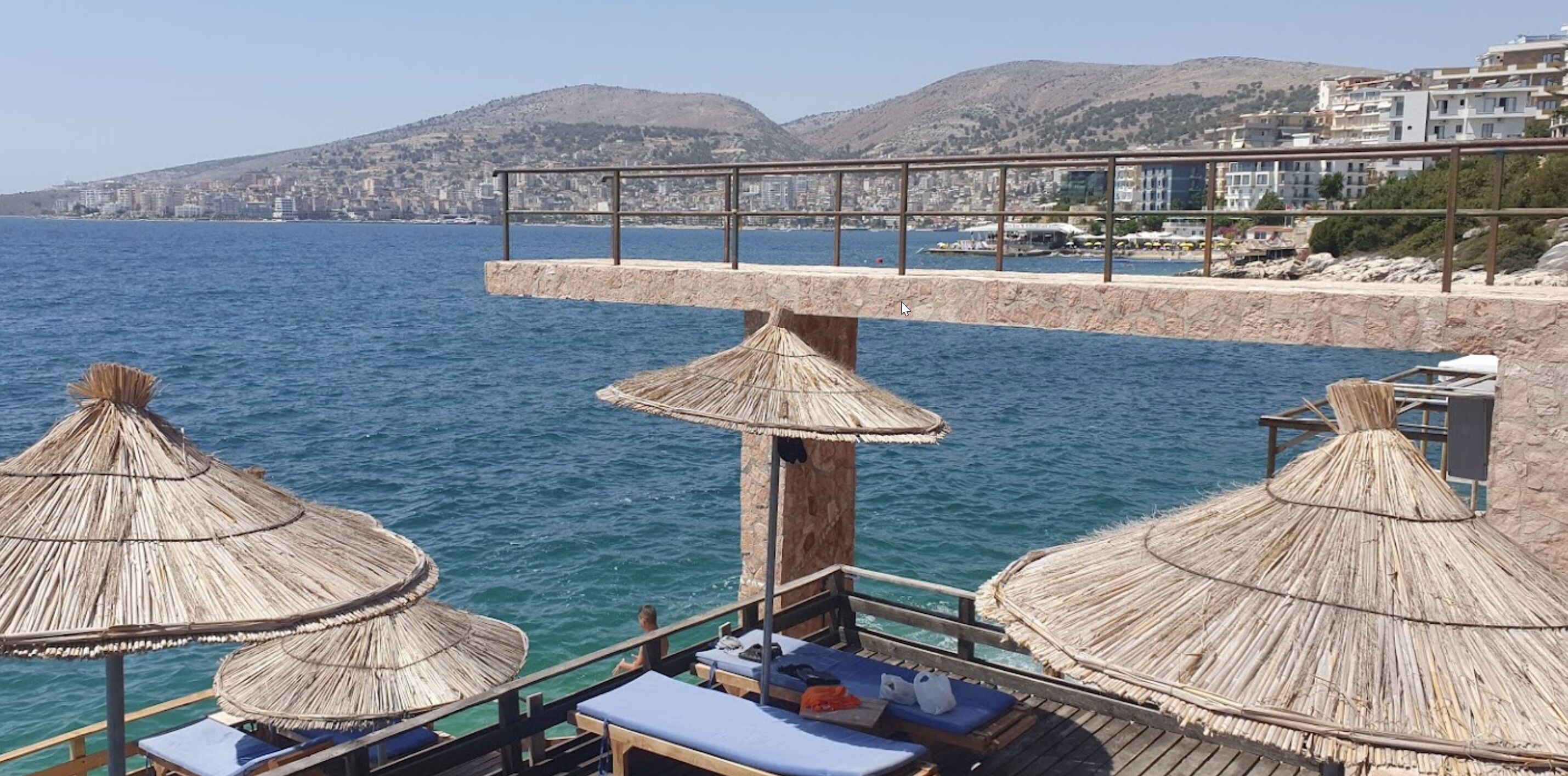 A seaside balcony with thatched umbrellas and lounge chairs overlooking the sea.