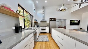 A modern kitchen with white cabinets, a central island, a stove, and a refrigerator. - Seascape - Kalbarri, WA (Kalbarri)