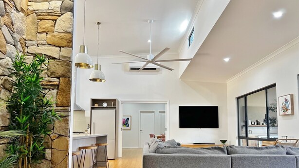 A modern living room with a stone accent wall, a grey sofa, a dining area with bar stools, and a flat-screen TV mounted on the wall. - Seascape - Kalbarri, WA (Kalbarri)