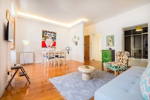 A living room with a wooden floor, a dining table with chairs, a sofa, a coffee table, and a painting on the wall. - Central Apartment at Chiado (Lisbon)