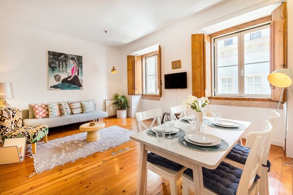 A dining area with a table set for four, a sofa, a painting, and a television on the wall. - Central Apartment at Chiado (Lisbon)