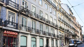 A street view of a building with a cafe named "A Carioca" on the ground floor, featuring large windows and a red door. - Central Apartment at Chiado (Lisbon)
