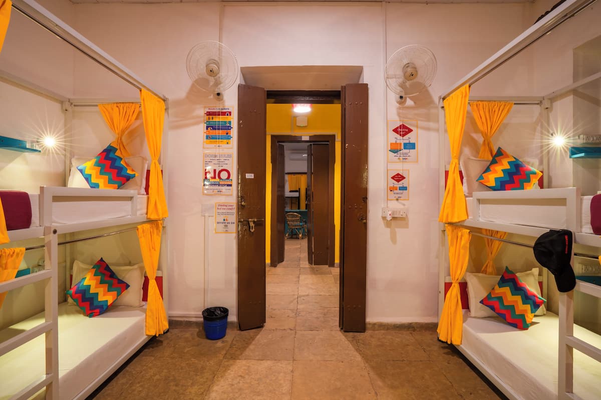 A hallway with bunk beds, each with colorful pillows and yellow curtains. There are signs on the walls and a door at the end of the hallway.