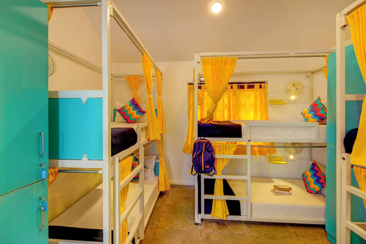 A dormitory room with bunk beds, yellow curtains, and a fan.