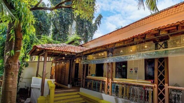 Une maison traditionnelle du Goa, dotée d’une véranda, d’un escalier et offrant une vue sur la végétation luxuriante environnante.
