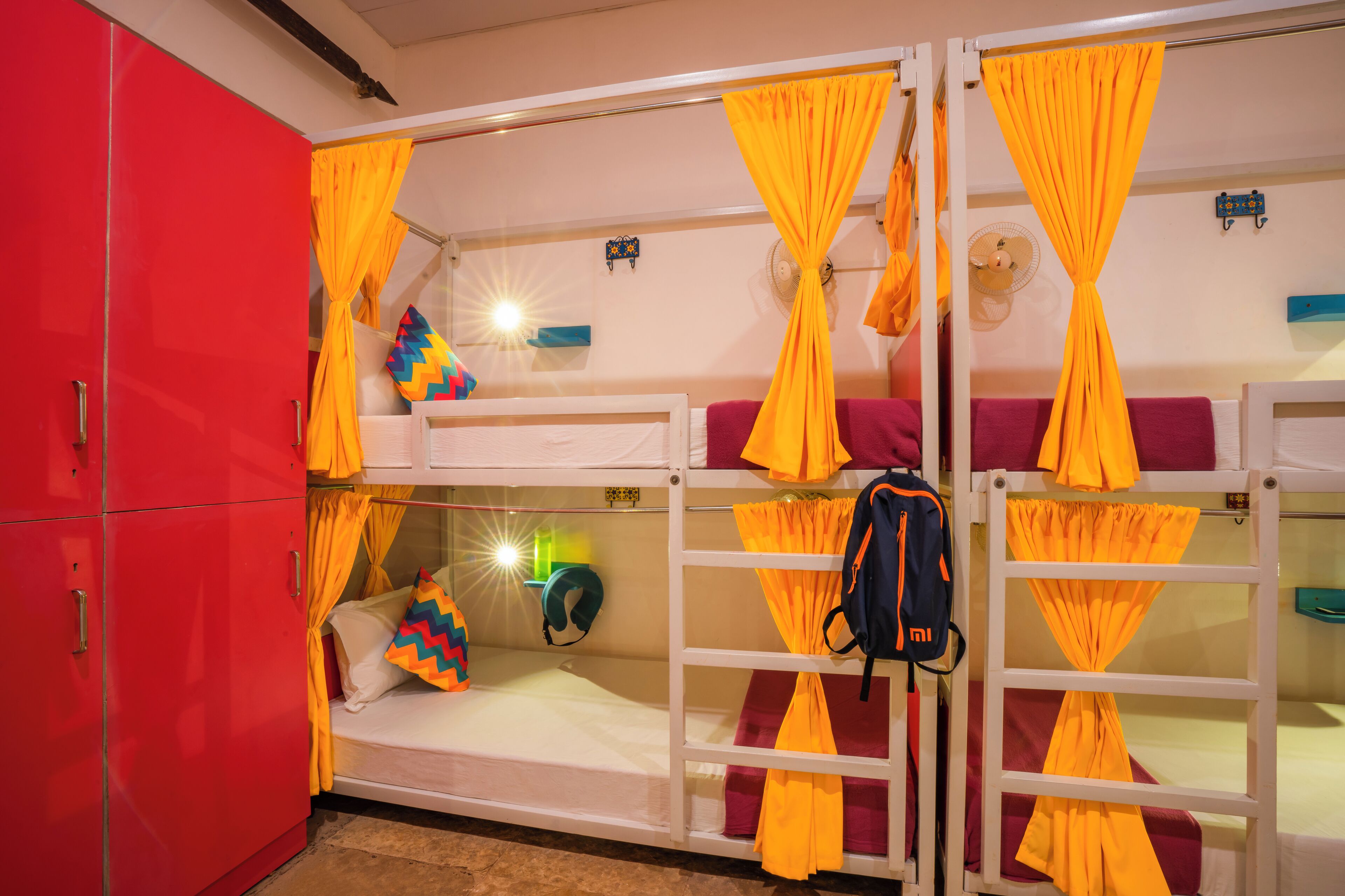 A bunk bed room with yellow curtains, a red wardrobe, and a fan on the wall.