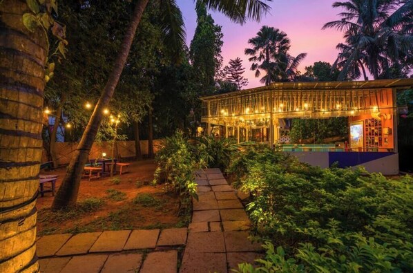 A well-lit outdoor area with a pool, surrounded by lush greenery and palm trees. - goSTOPS Lite Goa, Calangute (Calangute)