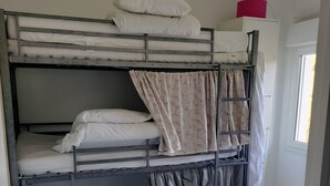 Een slaapkamer met een stapelbed, een bureau en stoel, een raam, en een roze voorwerp op het bureau.