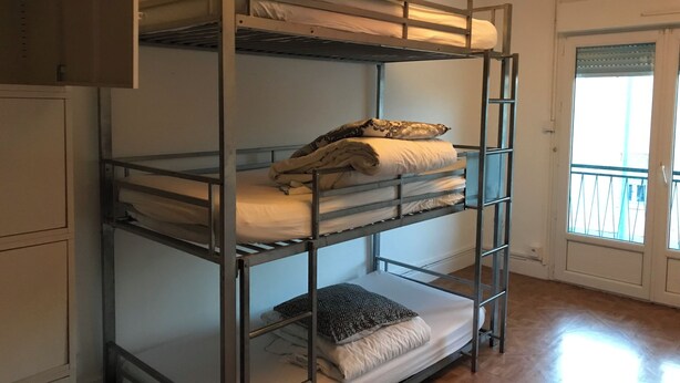 Een stapelbed met drie niveaus, een raam met zonwering en een deur met een handvat.