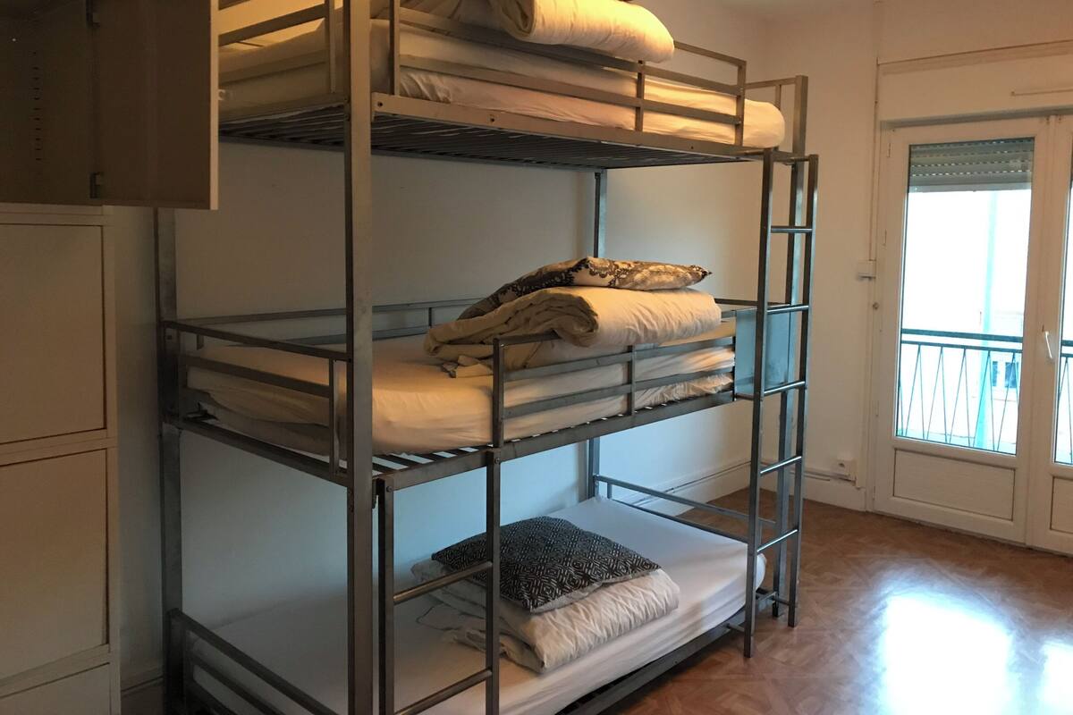 A bunk bed with three levels, a window with blinds, and a door with a handle.