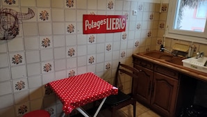 Een keuken met een betegelde spatwand, een rode tafel met stermotief, een houten kast en een raam met uitzicht.