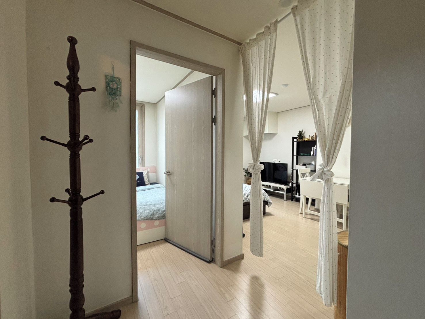 A hallway leading to a bedroom with a bed, a television, and a white chair.