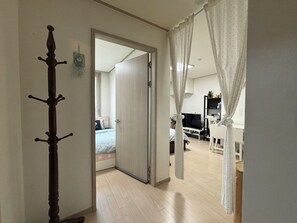 A hallway leading to a bedroom with a bed, a television, and a white chair.
