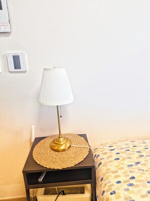 A bedside table with a lamp, a power outlet, and a wall-mounted thermostat. - Ansan City-View Apartment with Balcony (Ansan-si)