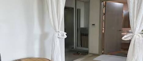 Un pasillo con piso de madera, cortinas blancas y una pequeña mesa redonda con un tirador.