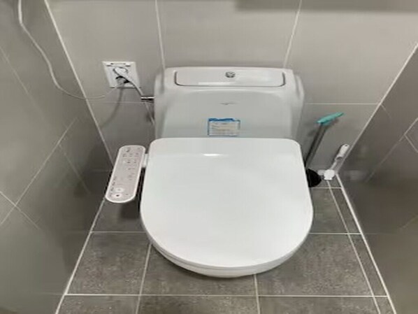 Une salle de bain avec des toilettes blanches, un panneau de commande et un sèche-mains.